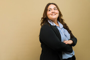 Beautiful Latin plus-size woman in professional attire confidently posing against a beige background