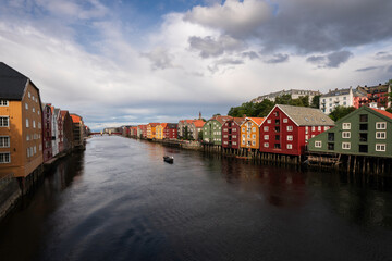 colorful houses of Trondheim Norway with boat cruising down the river Nidelven