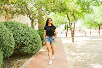 Confident latin woman in a stylish black t-shirt strolling through a sunny urban park, perfect for...