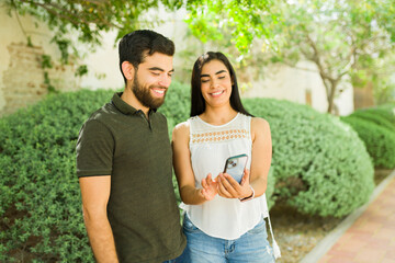 Happy young hispanic couple shares a joyful moment while looking at a smartphone together during their outdoor date
