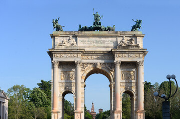 Porta Sempione with the Arco della Pace (arch of peace) triumphal arch and the towers of Castello Sforzeso (Sforza Castle) in the distance with blue sky on a late spring afternoon in Milan, Italy