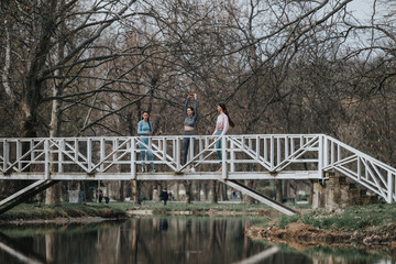Three women engaged in fitness activities on a picturesque bridge over a tranquil river in the park.