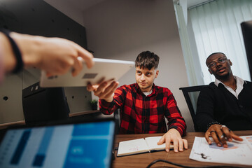 A dynamic, diverse team of young businesspeople engage in thoughtful discussion over documents in a modern office setting, highlighting teamwork and strategy.