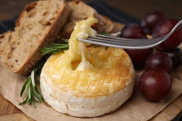 Taking tasty baked camembert with fork on table, closeup
