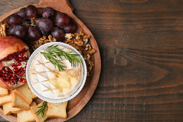 Board with tasty baked camembert, croutons, grapes, walnuts and pomegranate on wooden table, top view. Space for text
