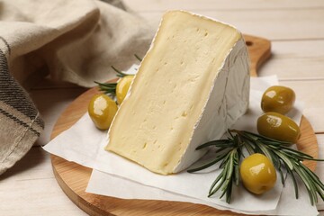 Board with piece of tasty camembert cheese, olives and rosemary on light wooden table, closeup