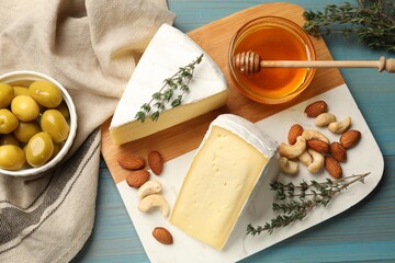 Tasty Camembert cheese with thyme, honey and nuts on light blue wooden table, flat lay