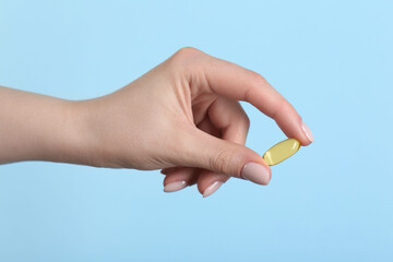Woman holding vitamin capsule on light blue background, closeup. Health supplement