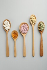 Different vitamin pills in spoons on light grey background, flat lay. Health supplement