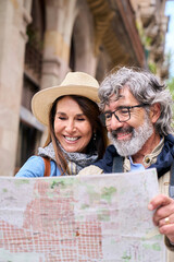Vertical. Mature couple in sixties smiling looking at map in European city street. Happy seniors...