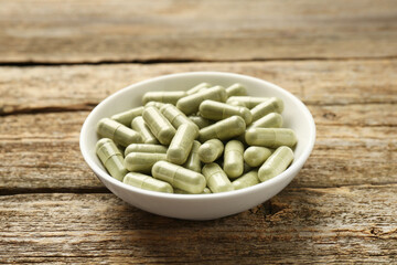 Vitamin capsules in bowl on wooden table, closeup
