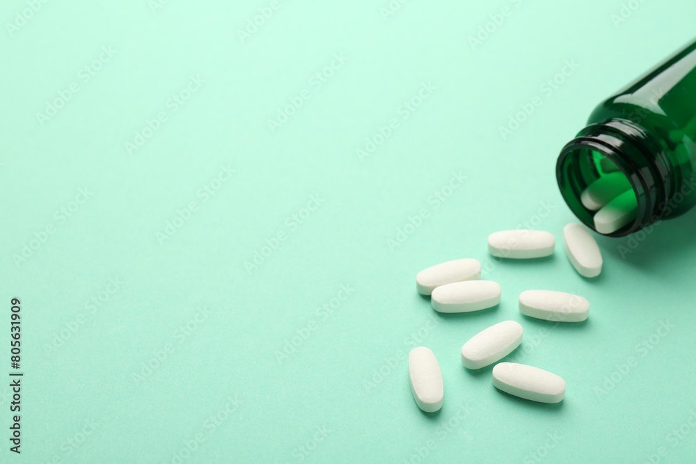 Wall mural Vitamin pills and bottle on mint color background. Space for text