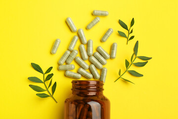 Vitamin pills, branches and bottle on yellow background, flat lay