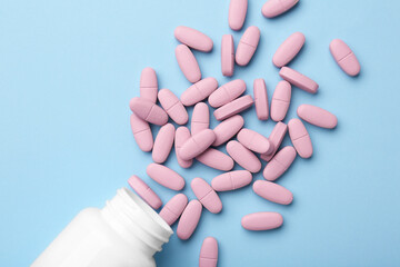 Vitamin pills and bottle on light blue background, top view