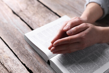 Religion. Christian woman praying over Bible at wooden table, closeup