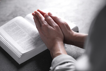 Religion. Christian woman praying over Bible at gray table, closeup