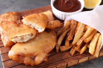 Tasty fish, chips and sauce on grey table, closeup