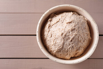 Fresh sourdough in proofing basket on wooden table, top view. Space for text