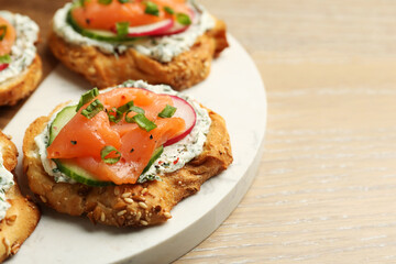 Tasty canapes with salmon, cucumber, radish and cream cheese on wooden table, closeup. Space for text