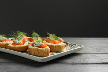 Tasty canapes with salmon, cucumber, cream cheese and dill on wooden table. Space for text