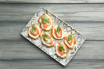 Tasty canapes with salmon, cucumber, cream cheese and dill on wooden table, top view