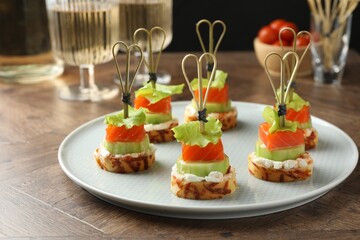Tasty canapes with salmon, cucumber, bread and cream cheese on wooden table