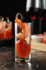 Tasty canape with shrimp, tomato and sauce in shot glass on black marble table, closeup