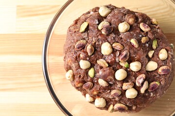 Raw chocolate dough with nuts in bowl on wooden table, top view