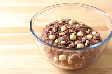 Raw chocolate dough with nuts in bowl on wooden table, closeup. Space for text
