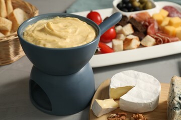 Fondue with tasty melted cheese and different snacks on grey table