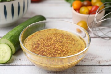 Tasty vinegar based sauce (Vinaigrette) in bowl and cucumber on wooden rustic table, closeup
