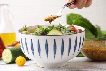 Woman pouring tasty vinegar based sauce (Vinaigrette) from spoon into bowl with salad at wooden...