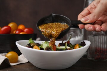 Woman pouring tasty vinegar based sauce (Vinaigrette) into bowl with salad at wooden table, closeup