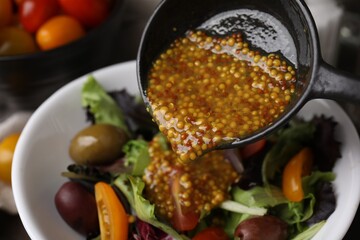 Pouring tasty vinegar based sauce (Vinaigrette) into bowl with salad, closeup
