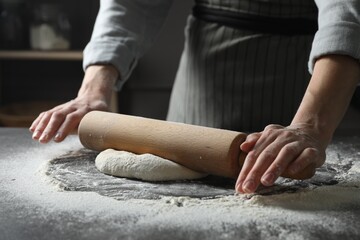 Woman rolling pizza dough with pin at table, closeup