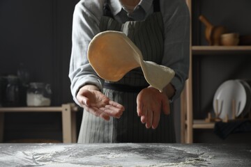 Woman tossing pizza dough at table in kitchen, closeup
