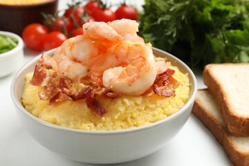 Fresh tasty shrimps, bacon and grits in bowl on white table, closeup