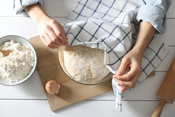 Woman covering dough with napkin at white wooden table, top view