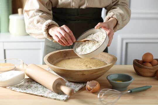 Making dough. Woman adding flour into bowl at wooden table in kitchen, closeup