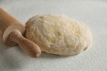 Raw dough and rolling pin on white table, closeup