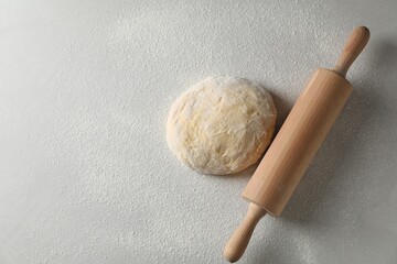 Raw dough and rolling pin on white table, top view. Space for text