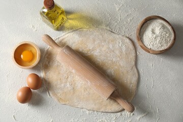 Raw dough, rolling pin and ingredients on table, flat lay