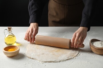 Woman rolling raw dough at table, closeup