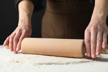 Woman rolling raw dough at table, closeup