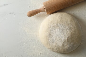 Raw dough and rolling pin on white marble table, above view. Space for text
