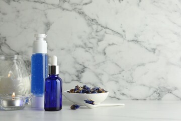 Spa composition. Bottles of cosmetic products, dry flowers and burning candles on white marble table, space for text