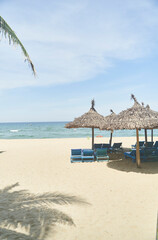 Straw sunshades and sunbeds on the empty pebble beach with sea in the background. Deserted beach with rattan sun loungers and umbrellas