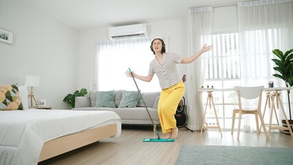 Smiling housekeeper with headphone listen music while cleaning floor. Happy caucasian mother...
