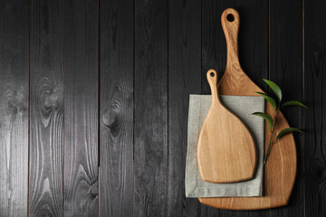 Cutting boards, green branch and napkin on black wooden table, top view. Space for text