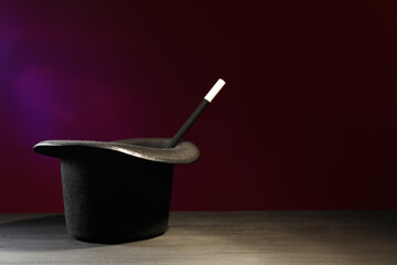 Magician's hat and wand on black wooden table against dark background, space for text